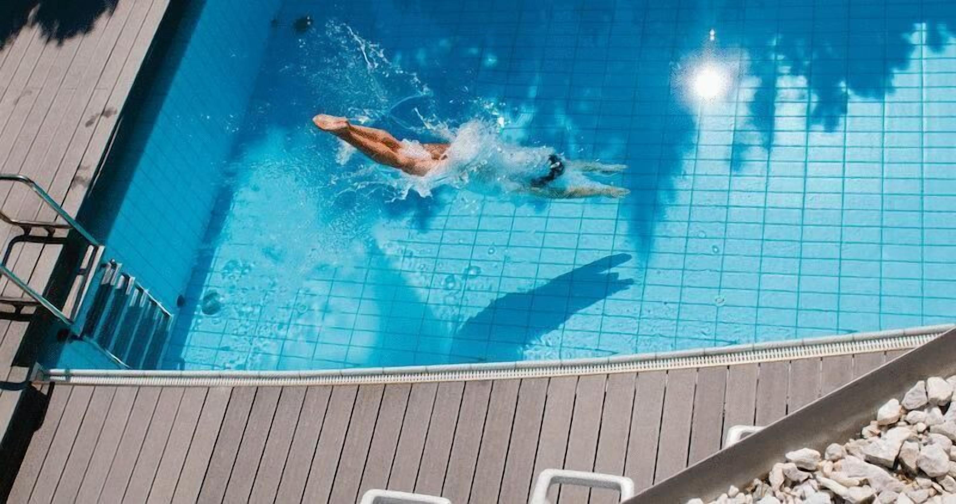 A swimming pool with a wooden deck and a metal ladder.