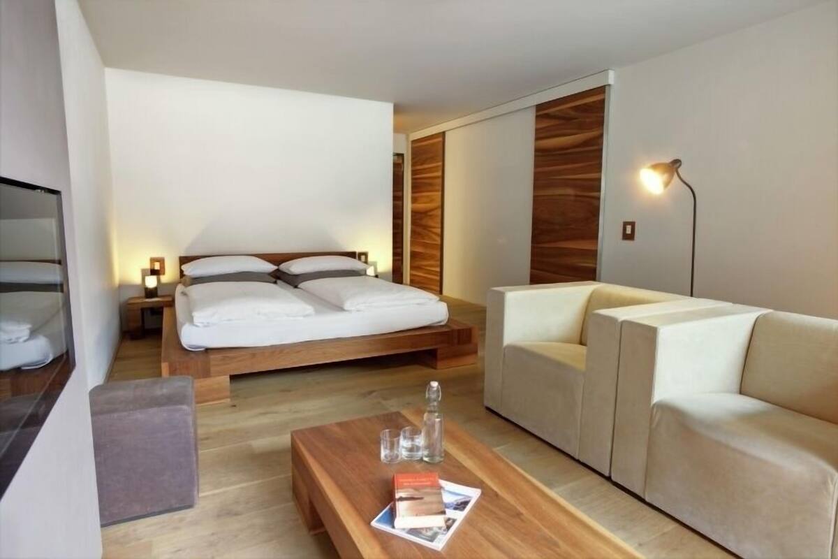 A modern hotel room with a bed, a sofa, a coffee table, and a lamp.