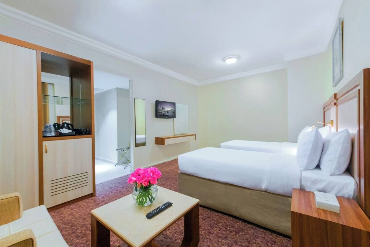 A hotel room with a bed, a desk with a remote control, a mirror, a television, and a small table with a vase of flowers.