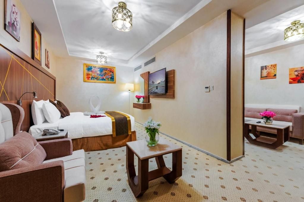 A hotel room with a bed, a sofa, a small table, a TV mounted on the wall, and artwork on the walls.