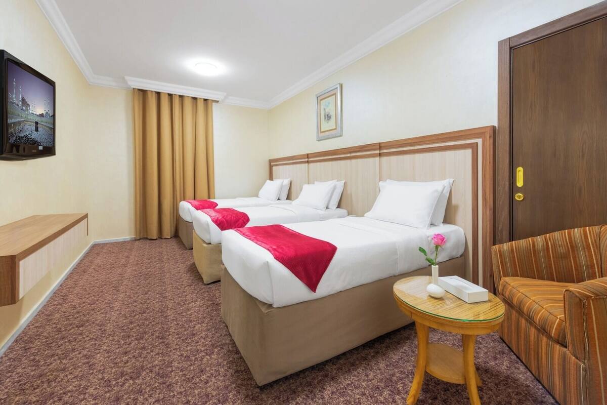 A hotel room with two beds, a small round table, a sofa, a TV, and a door.