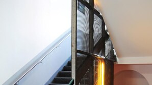 Una escalera con barandilla metálica, un panel de vidrio y un aplique de pared.