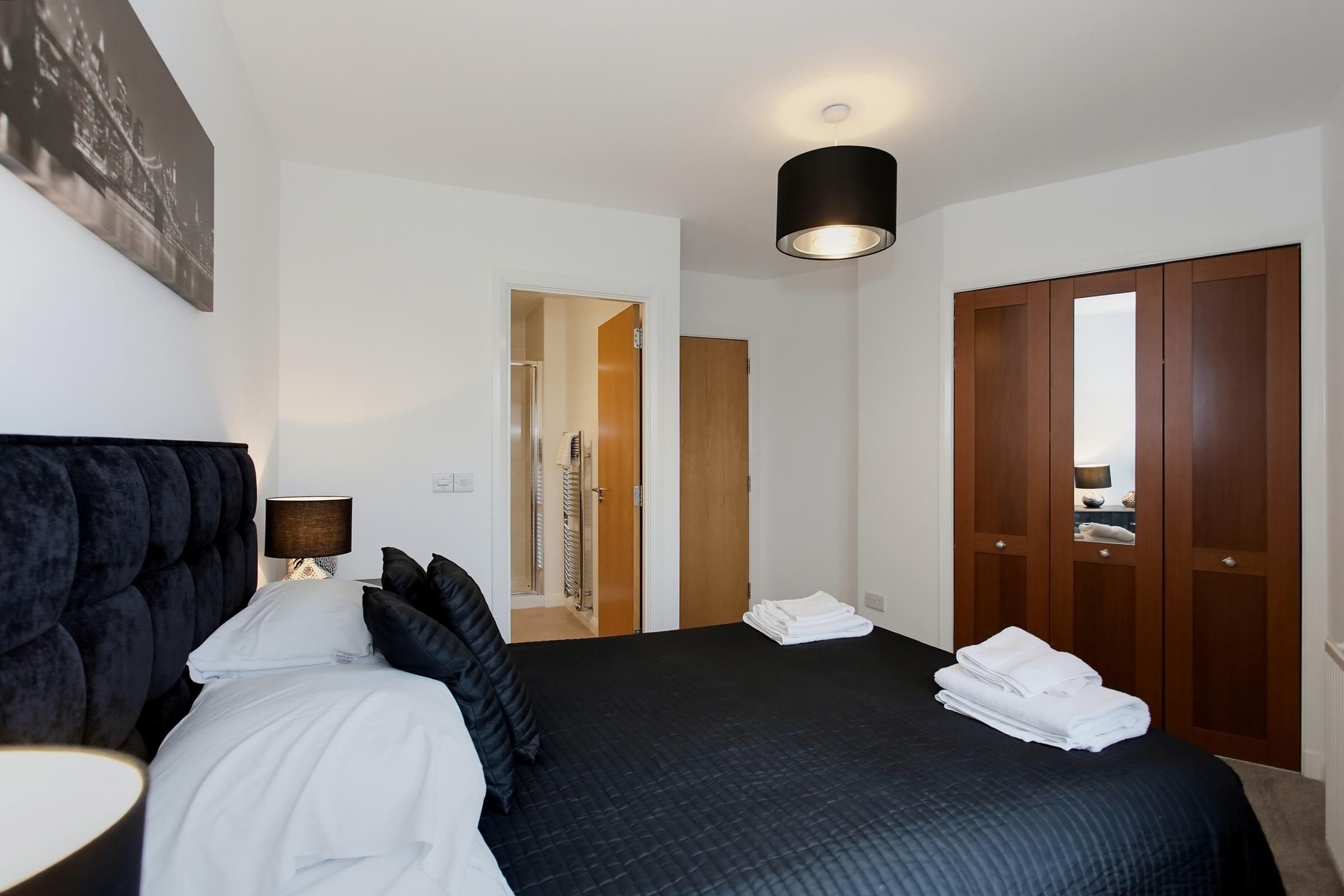 A hotel room with a large bed, a bedside table with a lamp, a wardrobe, and a shower area.