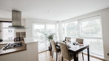 A modern kitchen with a gas stove, a built-in oven, and a stainless steel range hood. There is a dining table with chairs and a window with blinds.