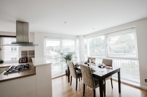 A modern kitchen with a gas stove, a built-in oven, and a stainless steel range hood. There is a dining table with chairs and a window with blinds. - Orange Apartments-Kepplestone (Aberdeen)