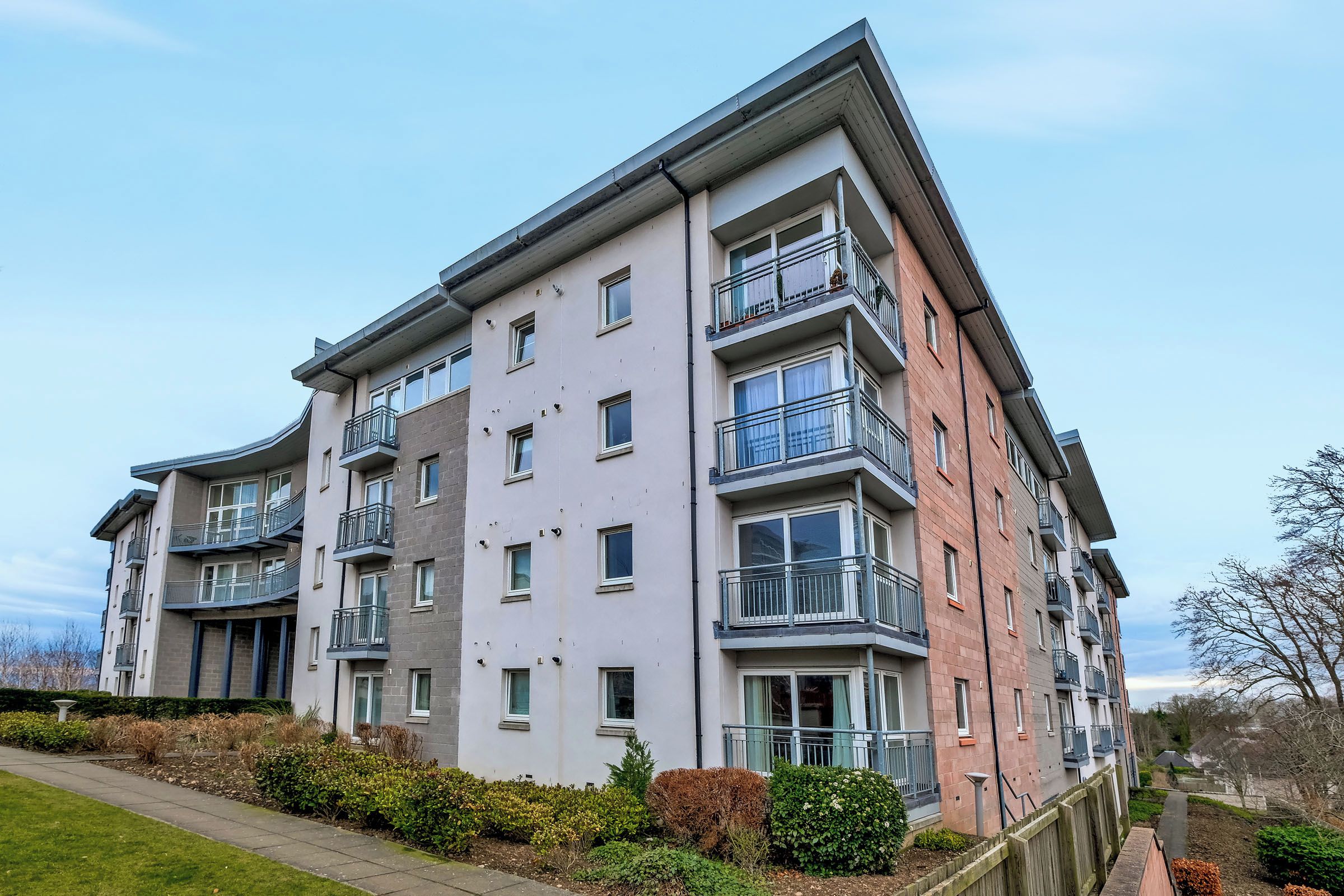 A multi-story residential building with balconies, a flat roof, and a gated entrance.