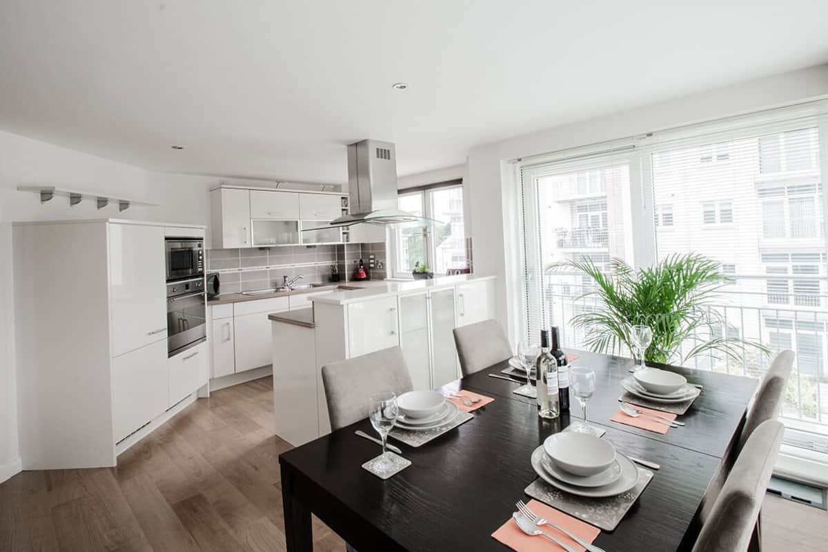 A modern kitchen with white cabinetry, a dining table set for four, and a large window with a view of buildings.