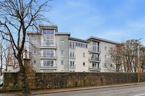 A multi-story residential building with a stone wall in front, a clear sky, and leafless trees. - Orange Apartments-Kepplestone (Aberdeen)