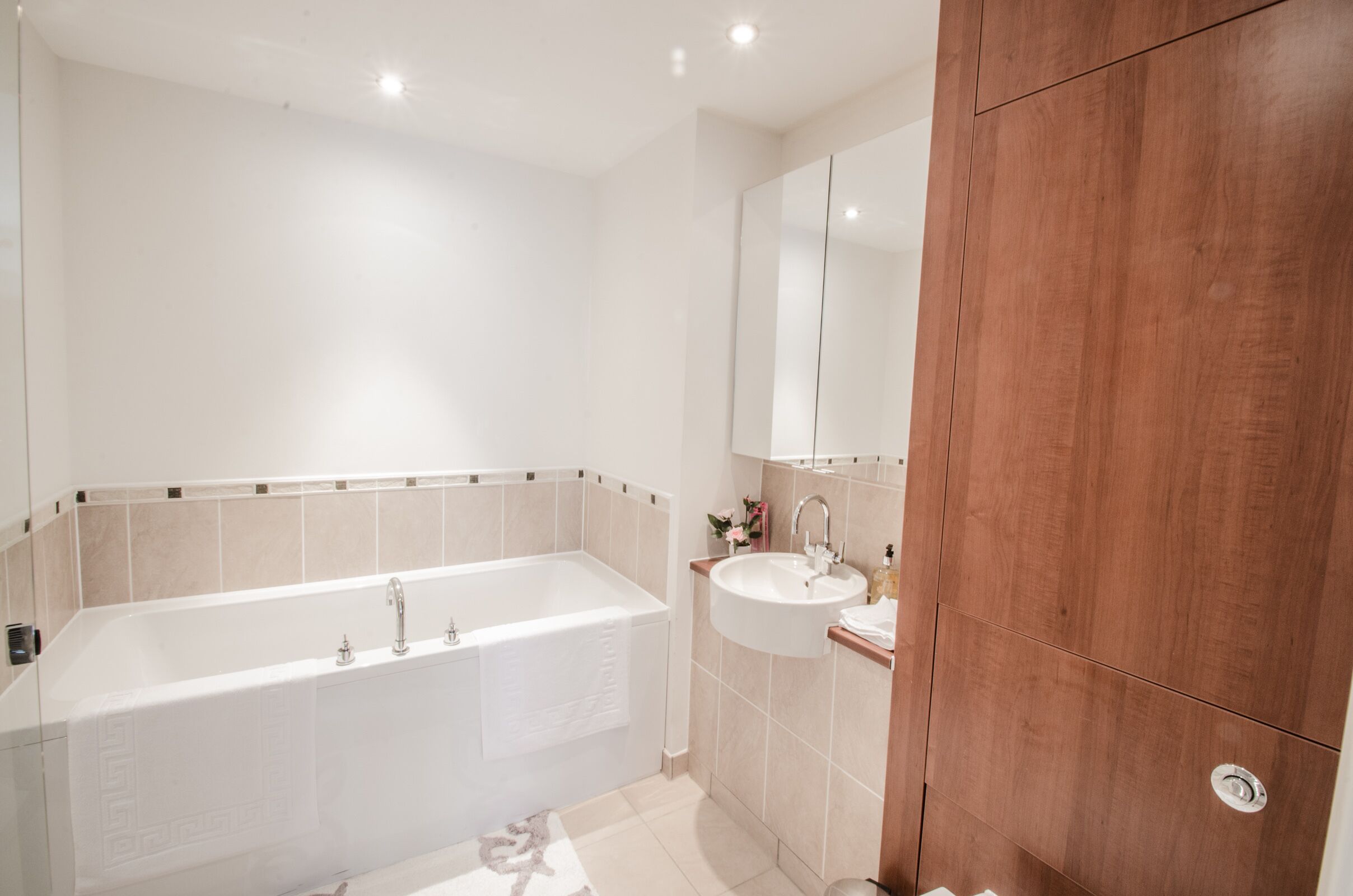 A modern bathroom with a bathtub, sink, and wooden cabinet.