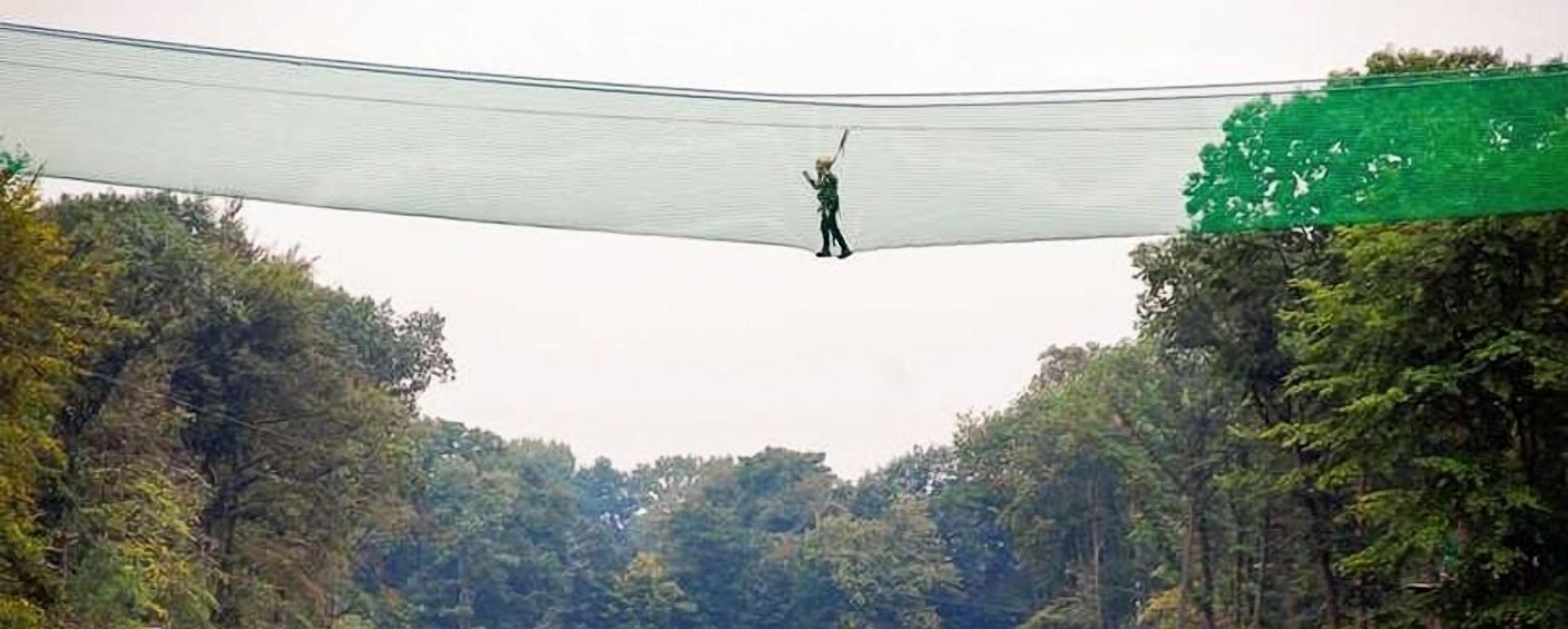 Eine Person geht über eine Hängebrücke in einem bewaldeten Gebiet.
