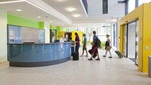 Een moderne receptie met een gebogen balie, een receptiemedewerker en een glazen deur naar buiten.