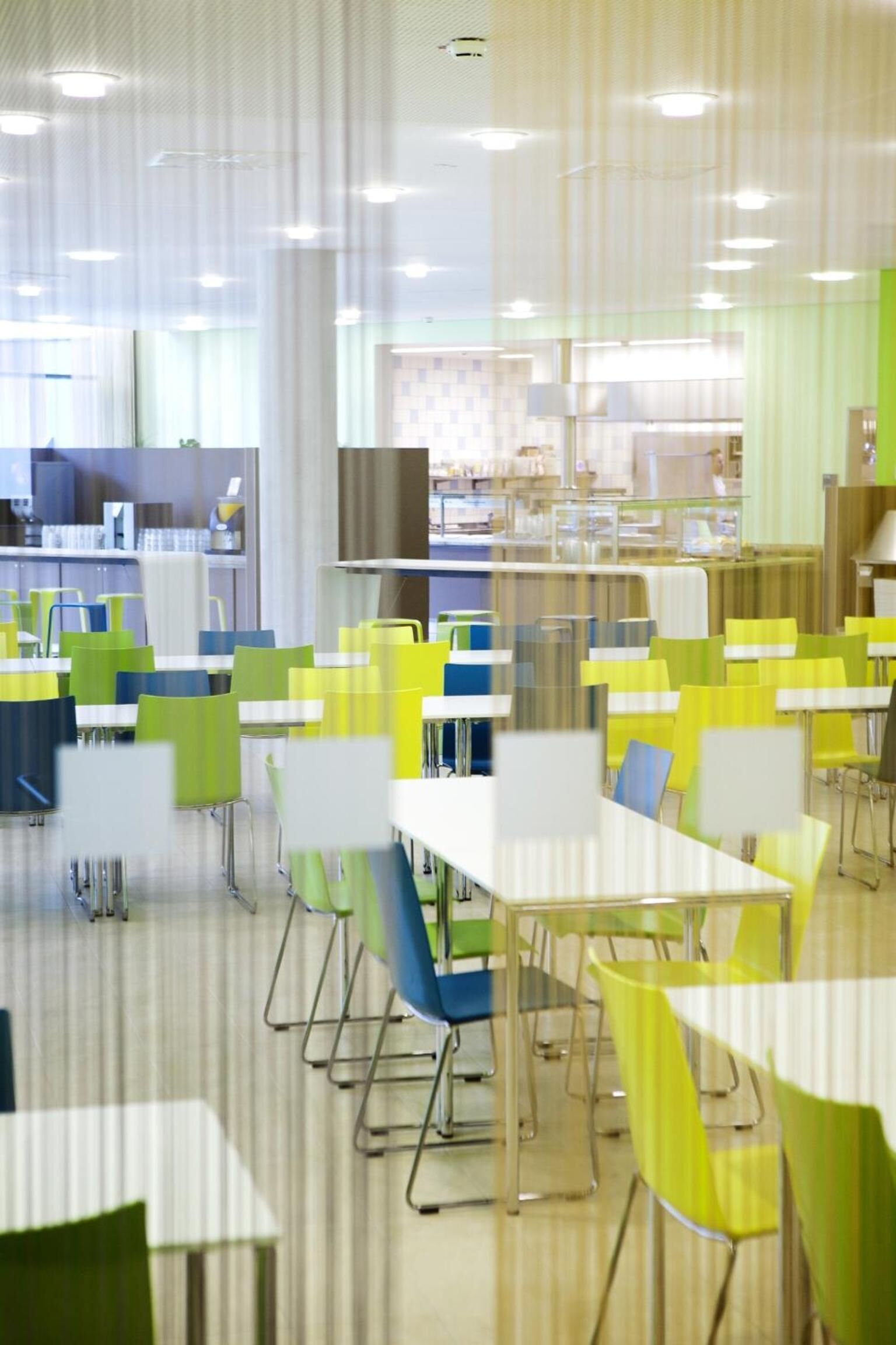 Eine Cafeteria mit mehreren Tischen und Stühlen, die in Reihen angeordnet sind.