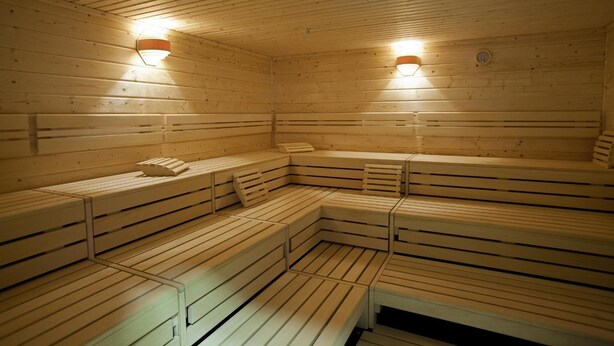 Un sauna avec des bancs en bois et deux lampes fixées au mur.