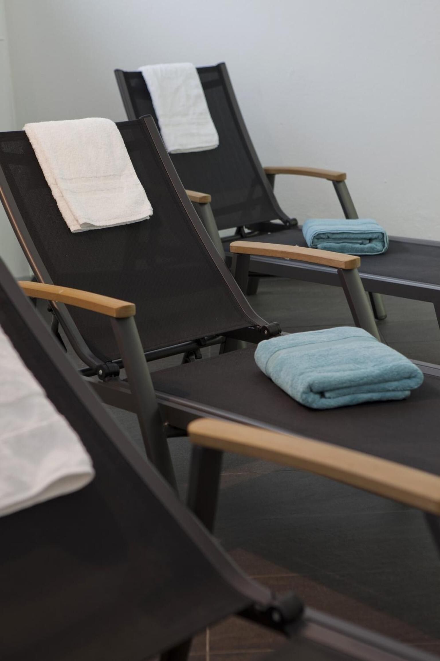 A row of black massage chairs with wooden armrests and towels placed on them.