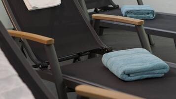 A row of black massage chairs with wooden armrests and towels placed on them.