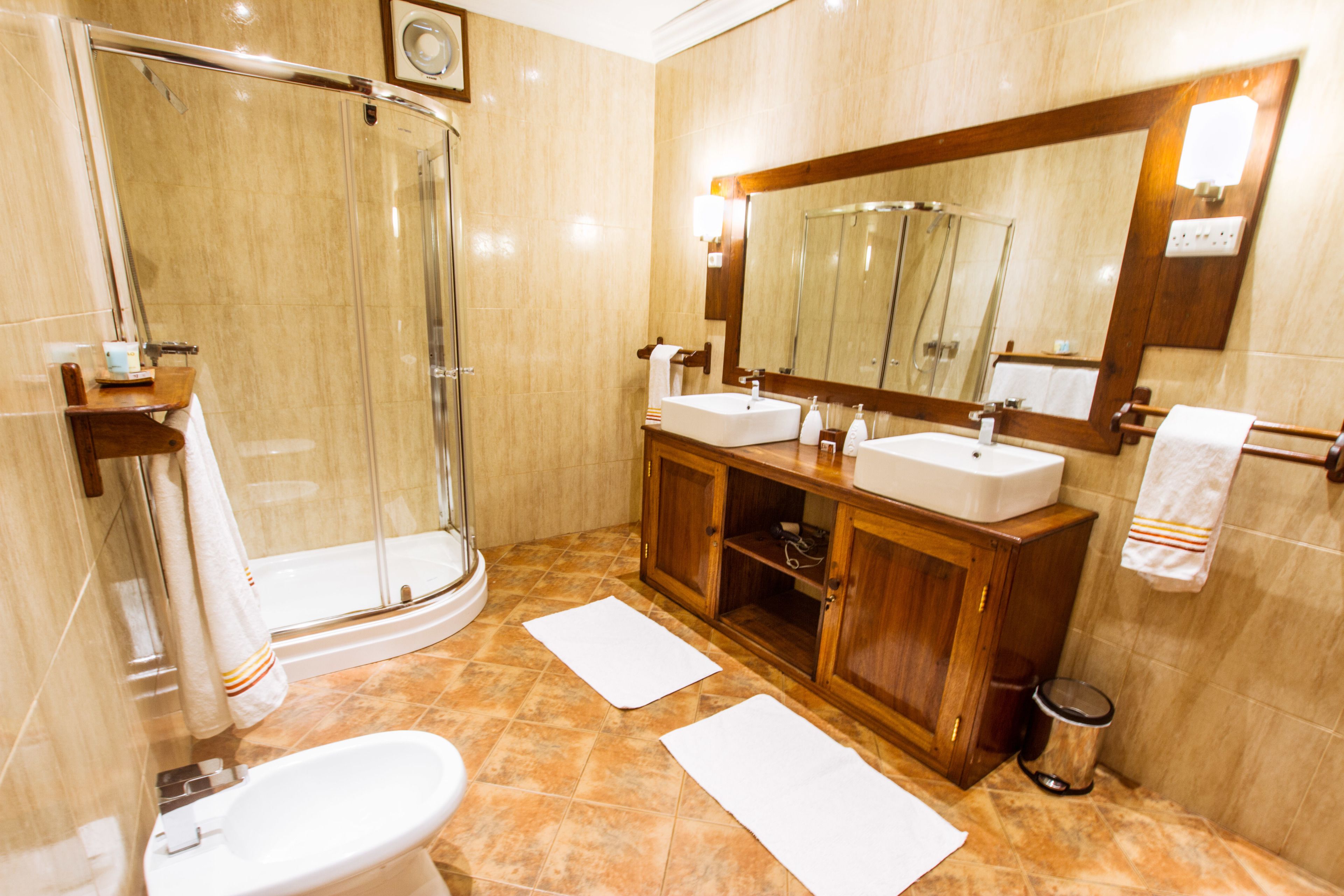 Ein Badezimmer mit einer gläsernen Duschkabine, zwei Waschbecken, einer Toilette und einem großen Spiegel.