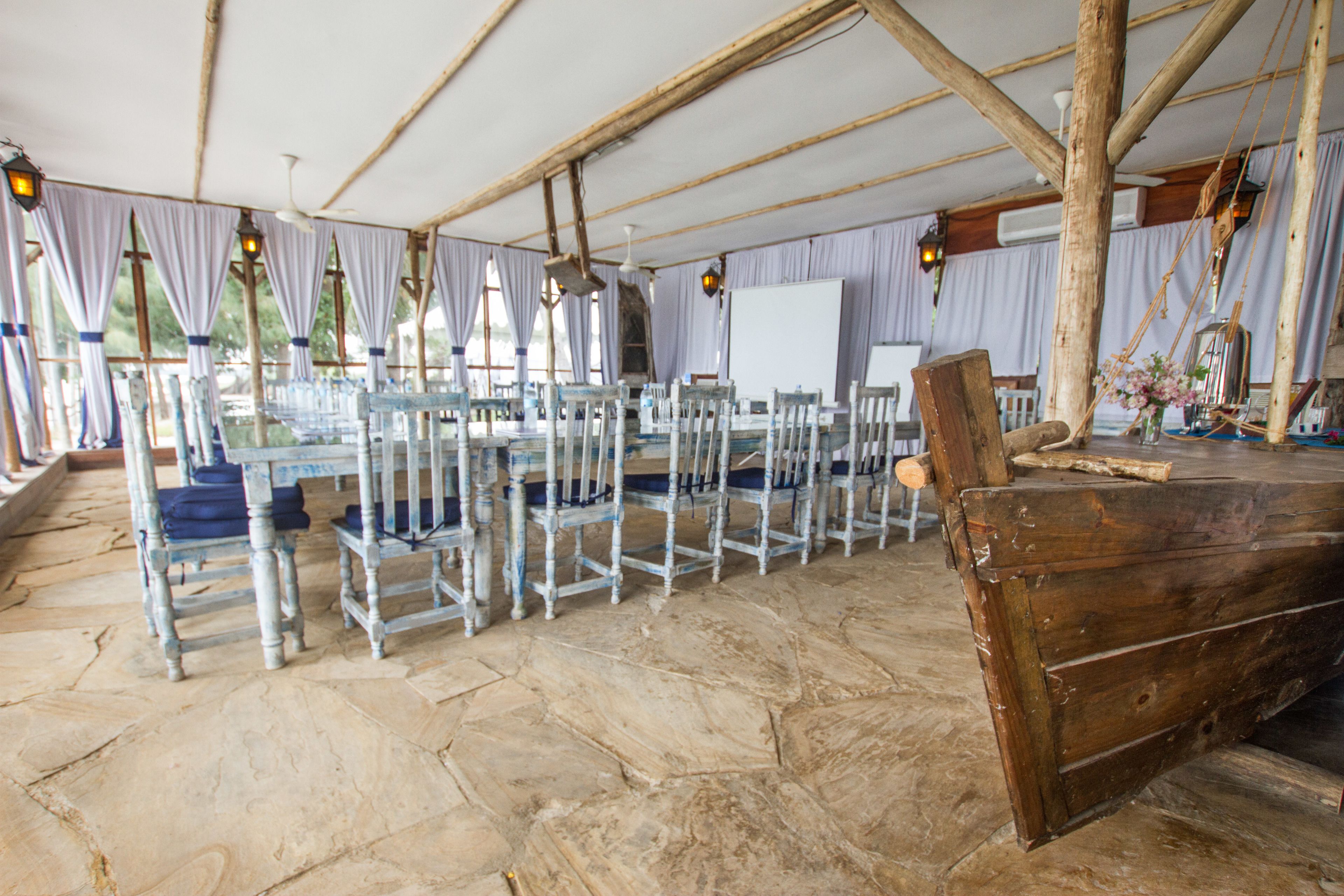 A rustic wooden boat in a covered outdoor area with stone flooring, metal chairs, and a whiteboard.
