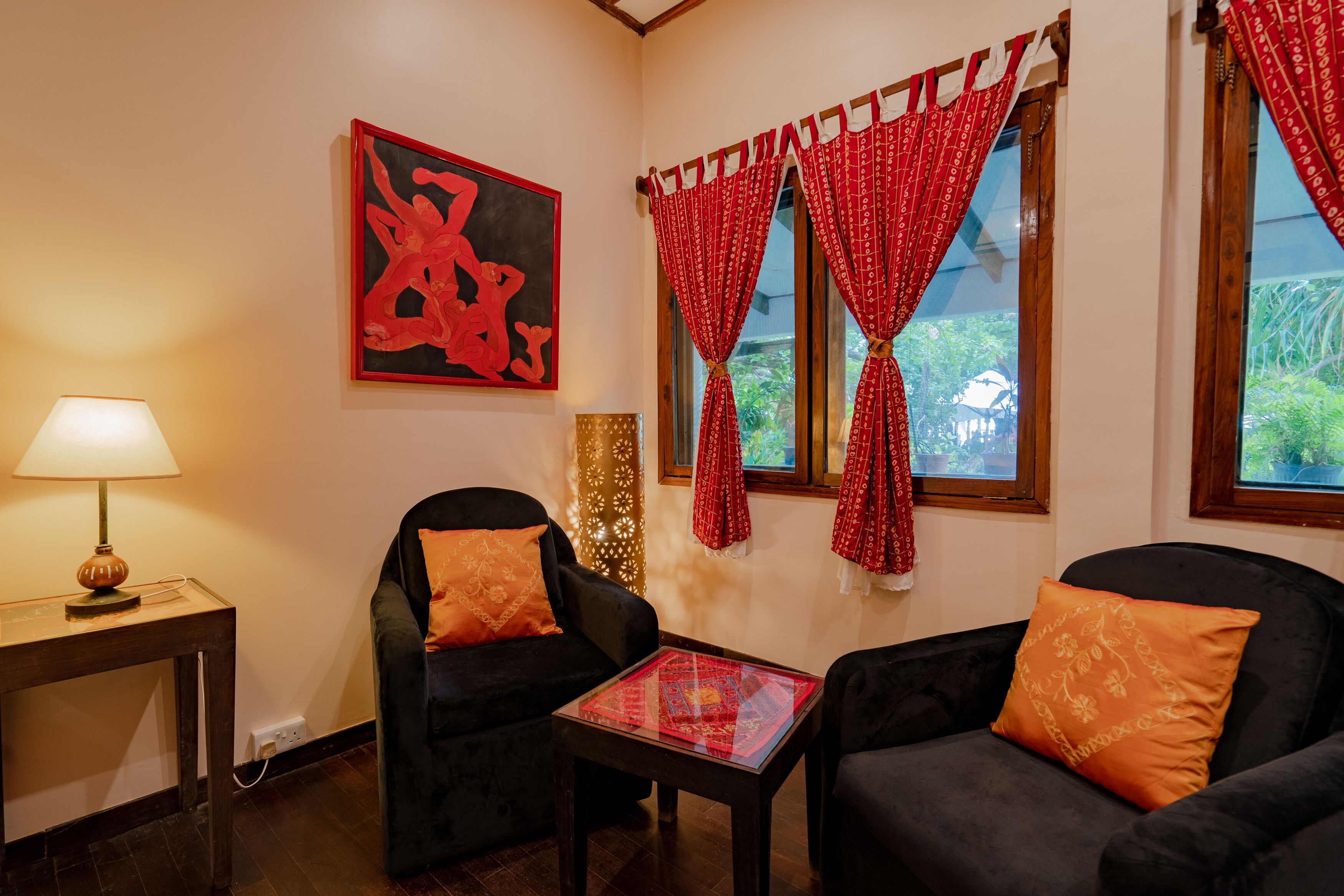 A room with two black armchairs, a small table, a lamp, a red and white patterned curtain, and a large abstract painting on the wall.