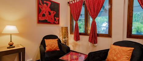 A room with two black armchairs, a small table, a lamp, a red and white patterned curtain, and a large abstract painting on the wall.