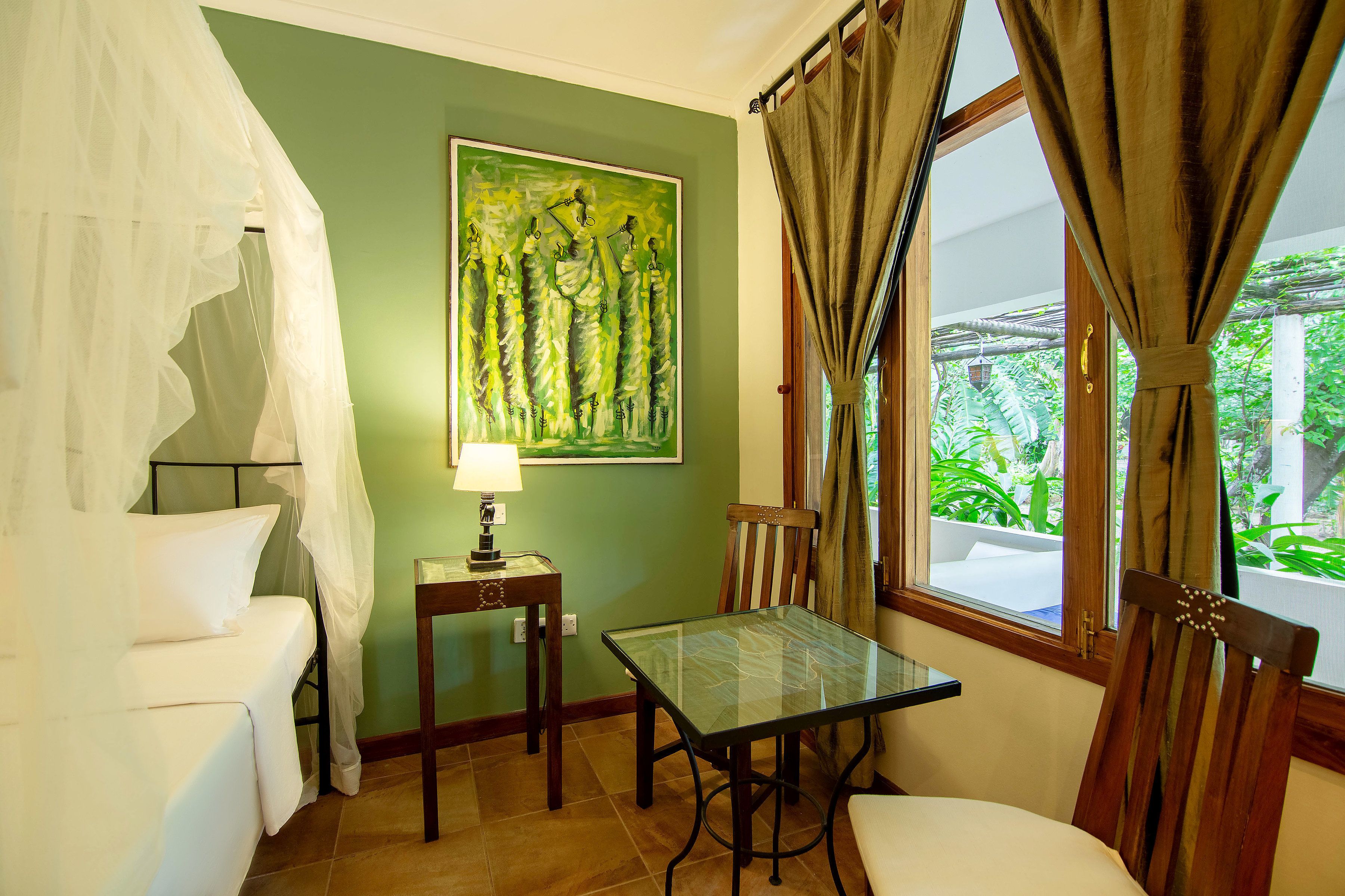 A room with a bed, a table, a chair, a lamp, and a painting on the wall.