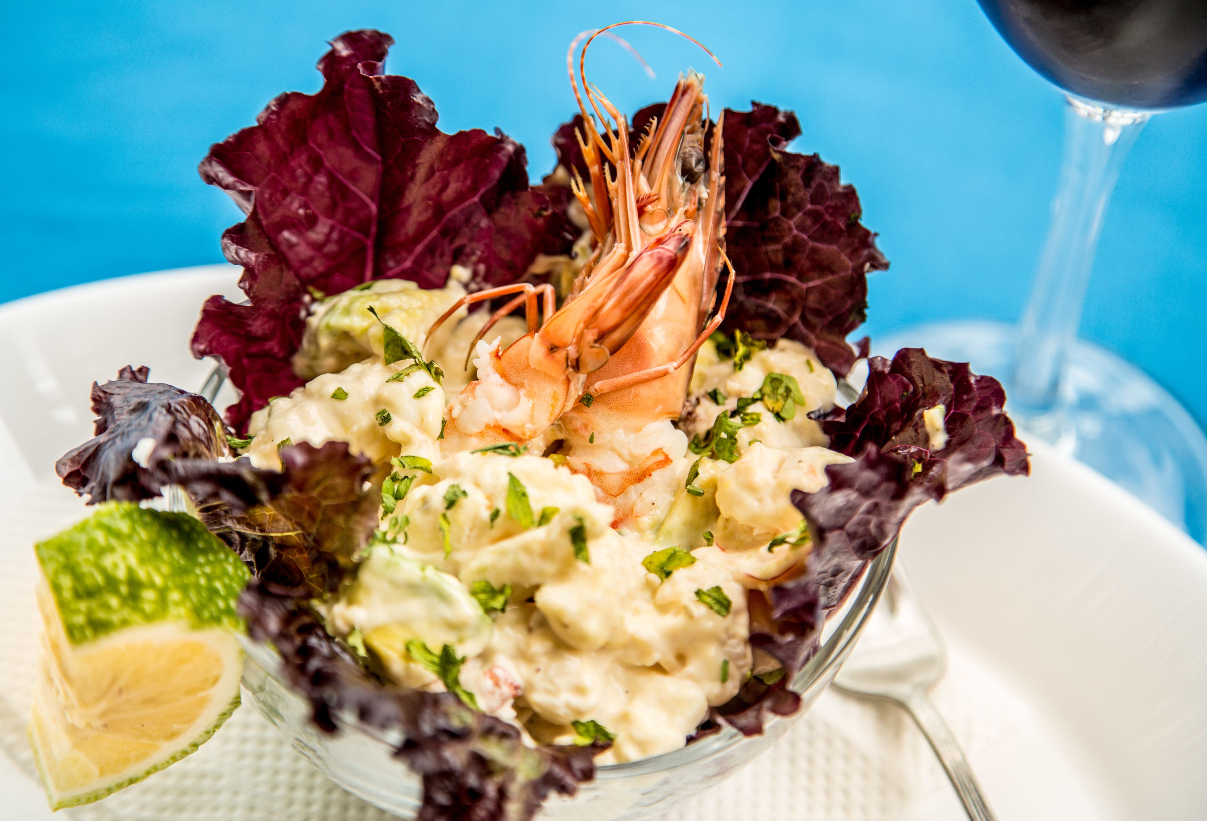 A seafood salad with a shrimp centerpiece, garnished with herbs, served in a clear bowl.