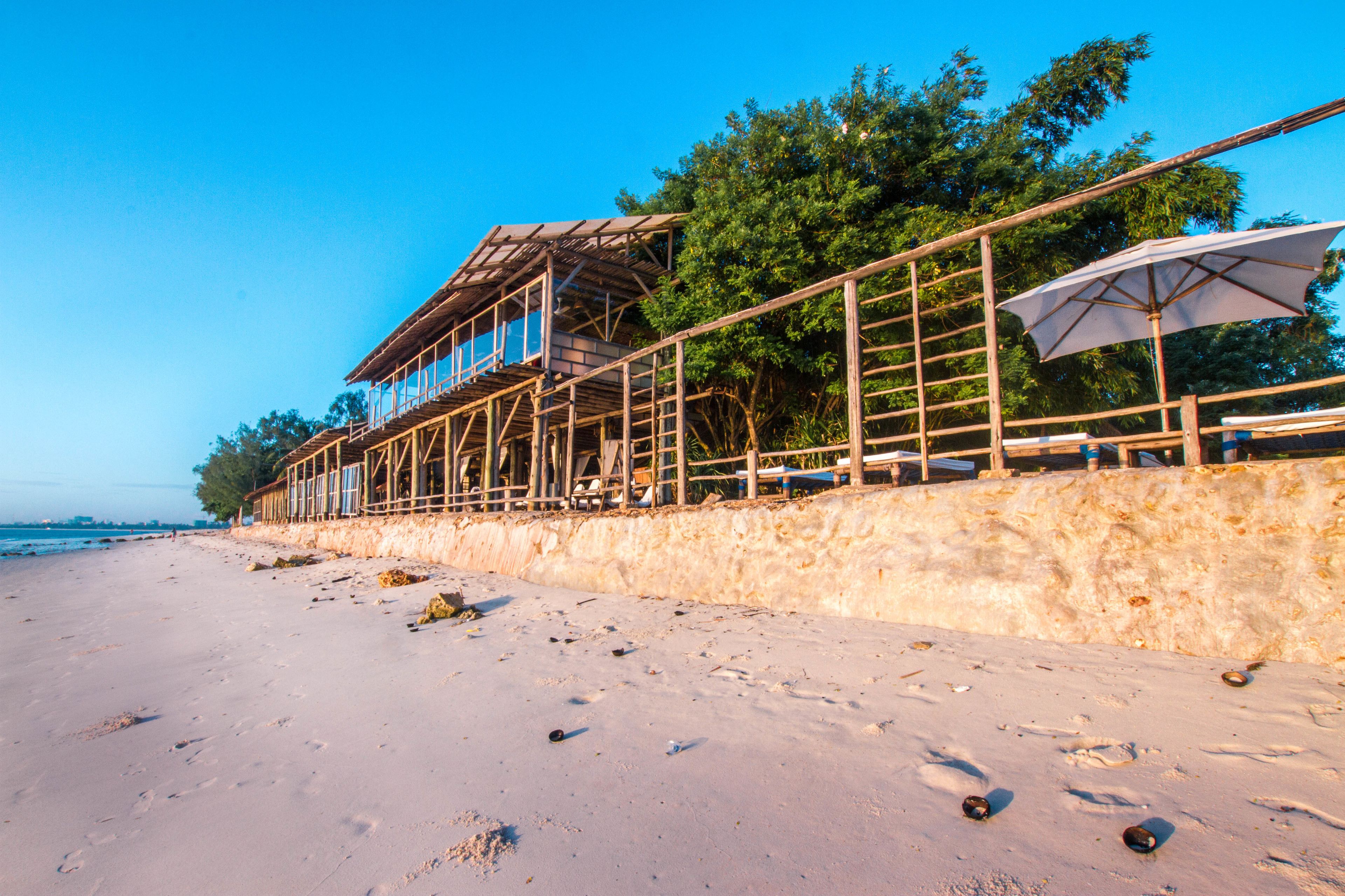 A beachside wooden structure with a balcony overlooking the sea, a sandy beach, and a clear blue sky.
