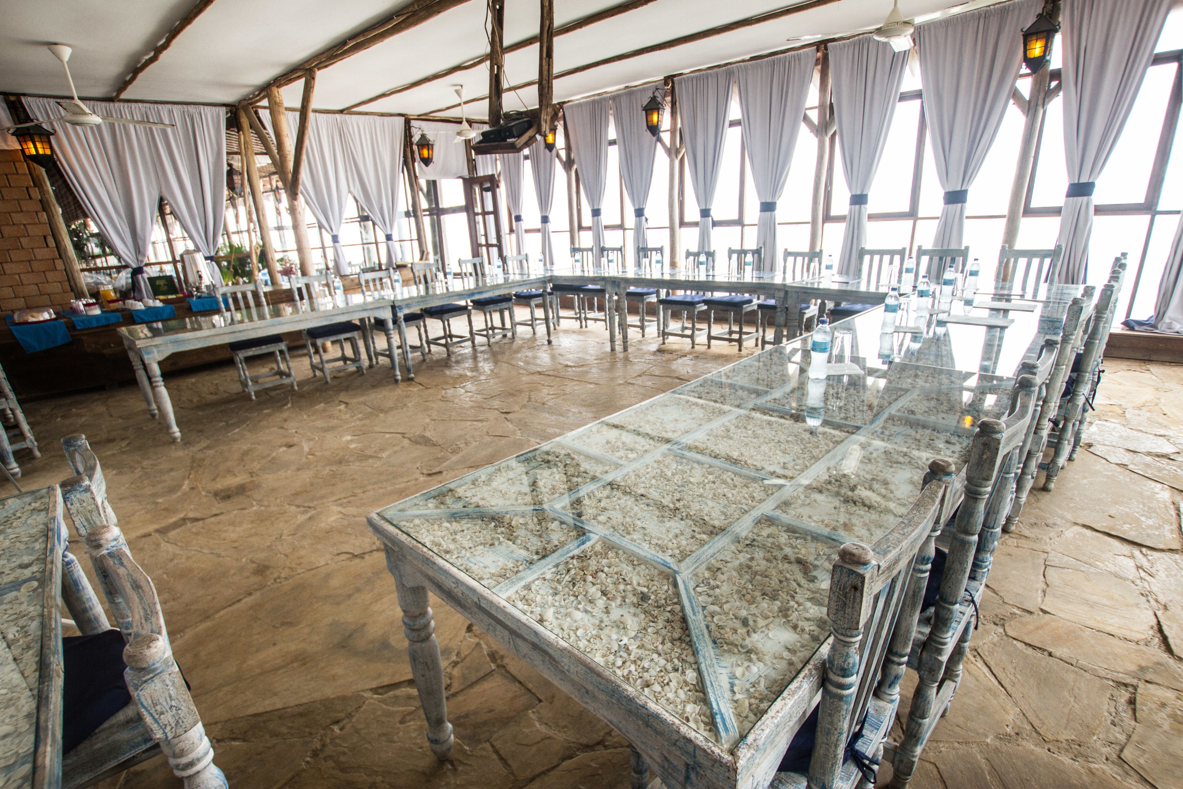 A large, rustic dining hall with stone flooring and wooden tables and chairs.