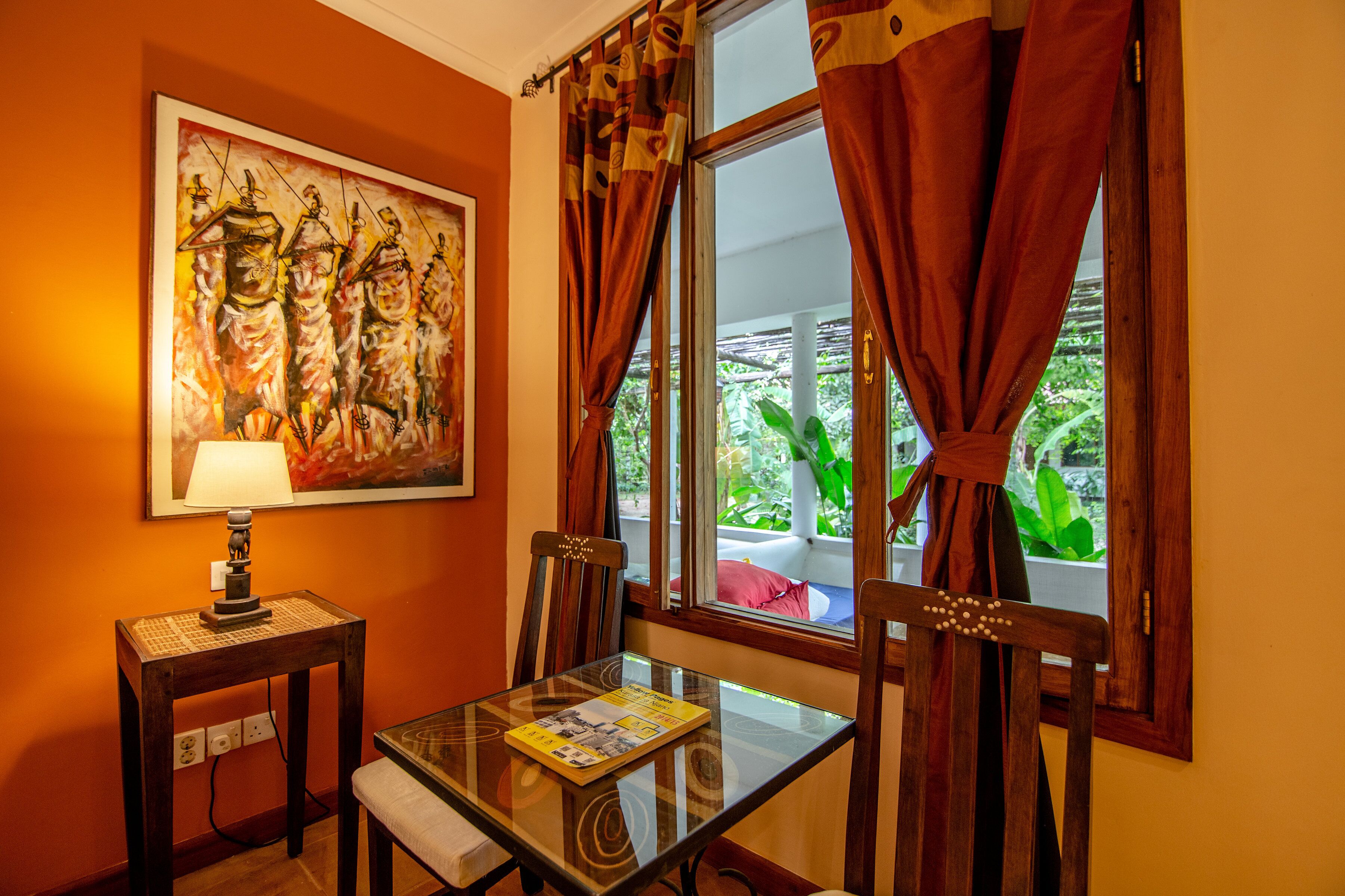 A dining area with a table, chairs, a lamp, and a painting on the wall.