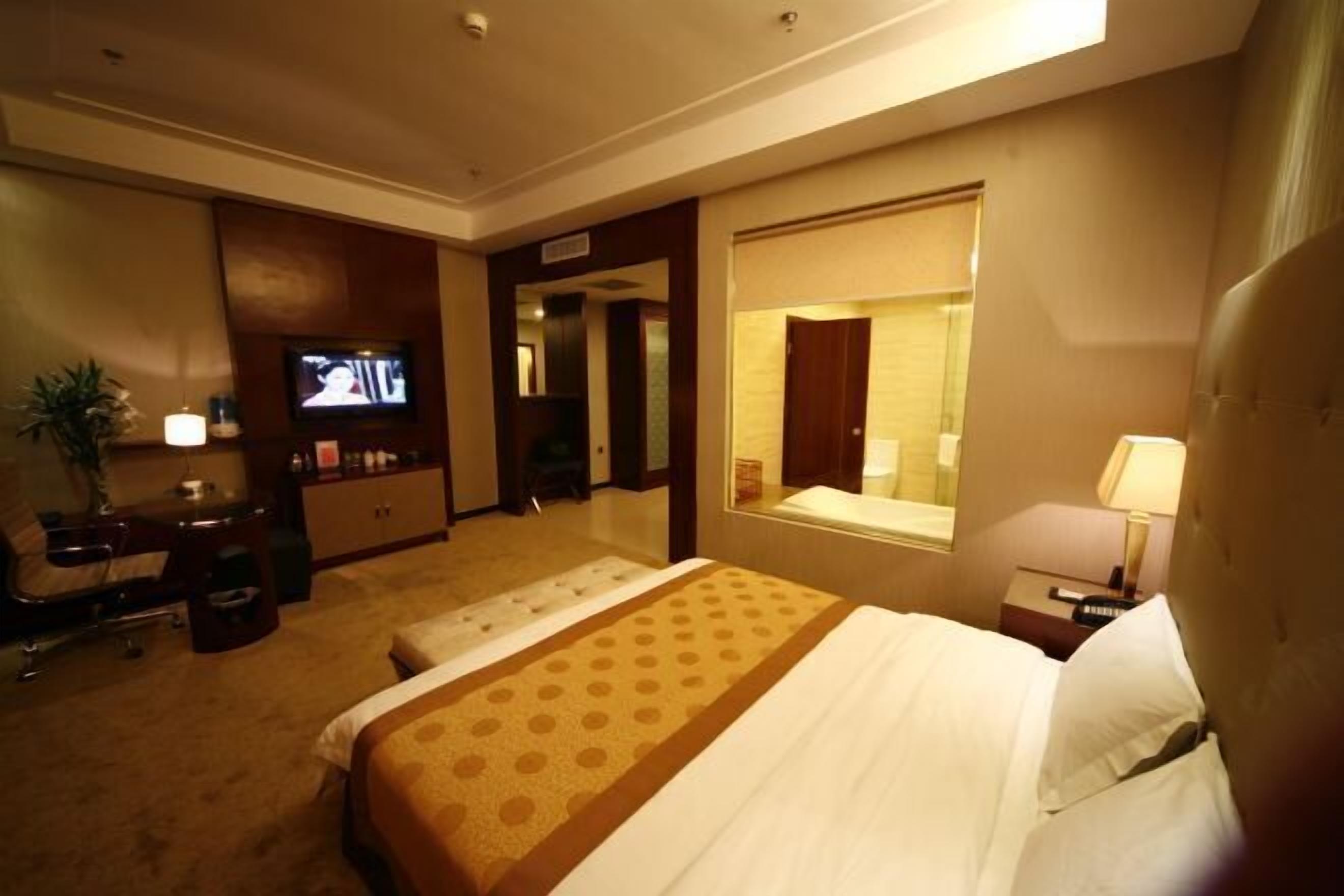 Habitación de hotel con una cama grande, un escritorio con una computadora, un televisor y una ventana.