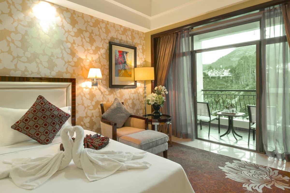 A hotel room with a bed, a chair, a small table with a lamp, and a balcony with a table and chairs.