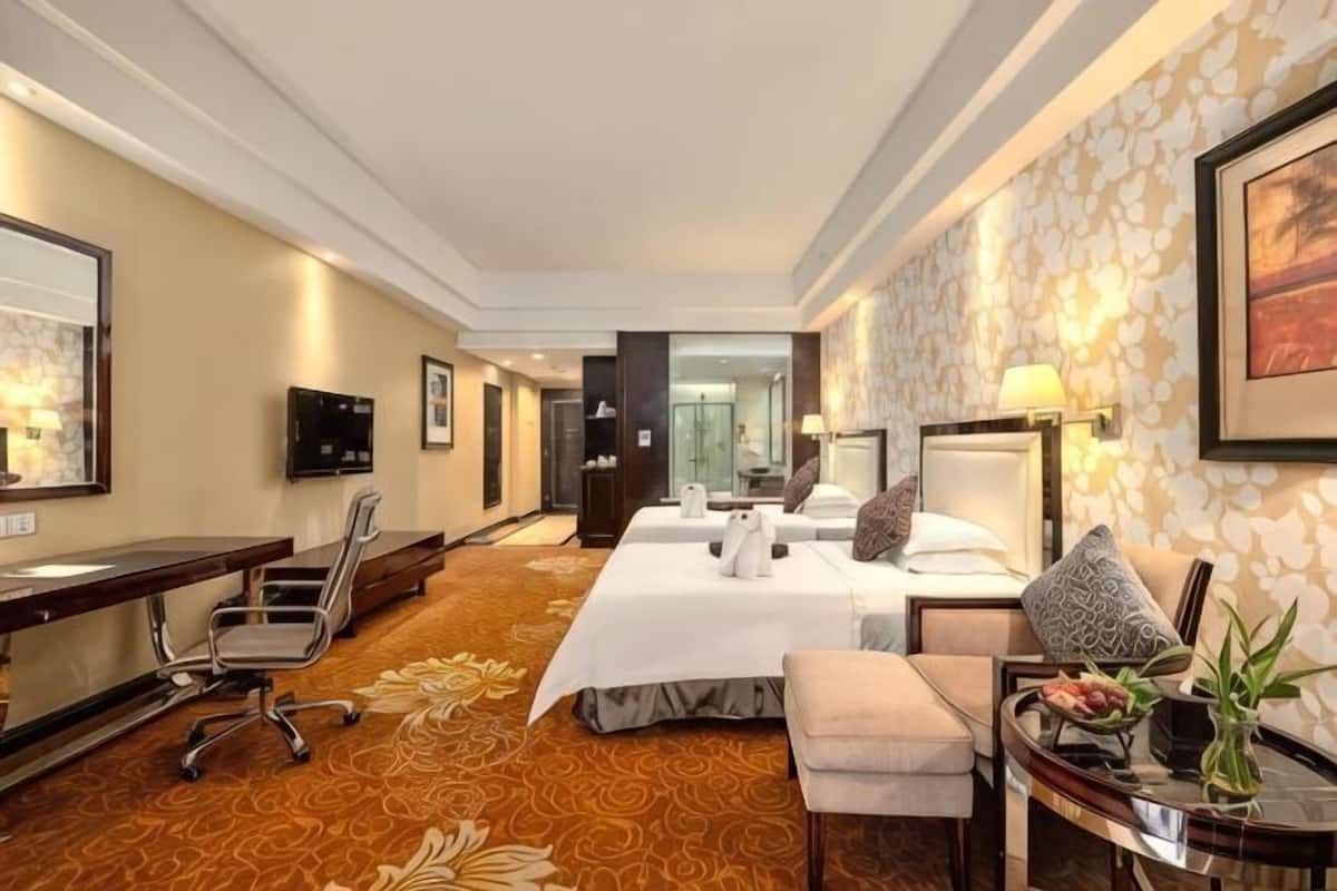 A hotel room with a large bed, a desk, a chair, a small table with a vase, and a television.