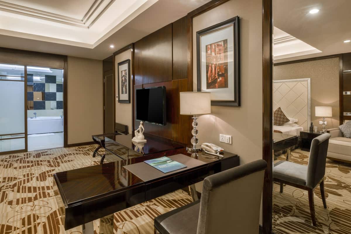 A hotel room with a large desk, a flat-screen TV, a lamp, a telephone, a sofa, and a bed.