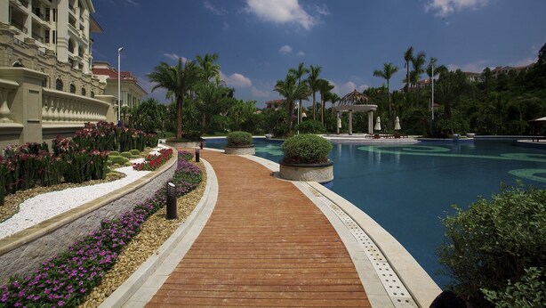 A resort pool area with a wooden walkway, palm trees, and a large building in the background. - Country Garden Phoenix Hotel Huiyang (Huizhou)