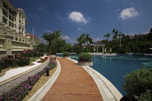 A resort pool area with a wooden walkway, palm trees, and a large building in the background. - Country Garden Phoenix Hotel Huiyang (Huizhou)