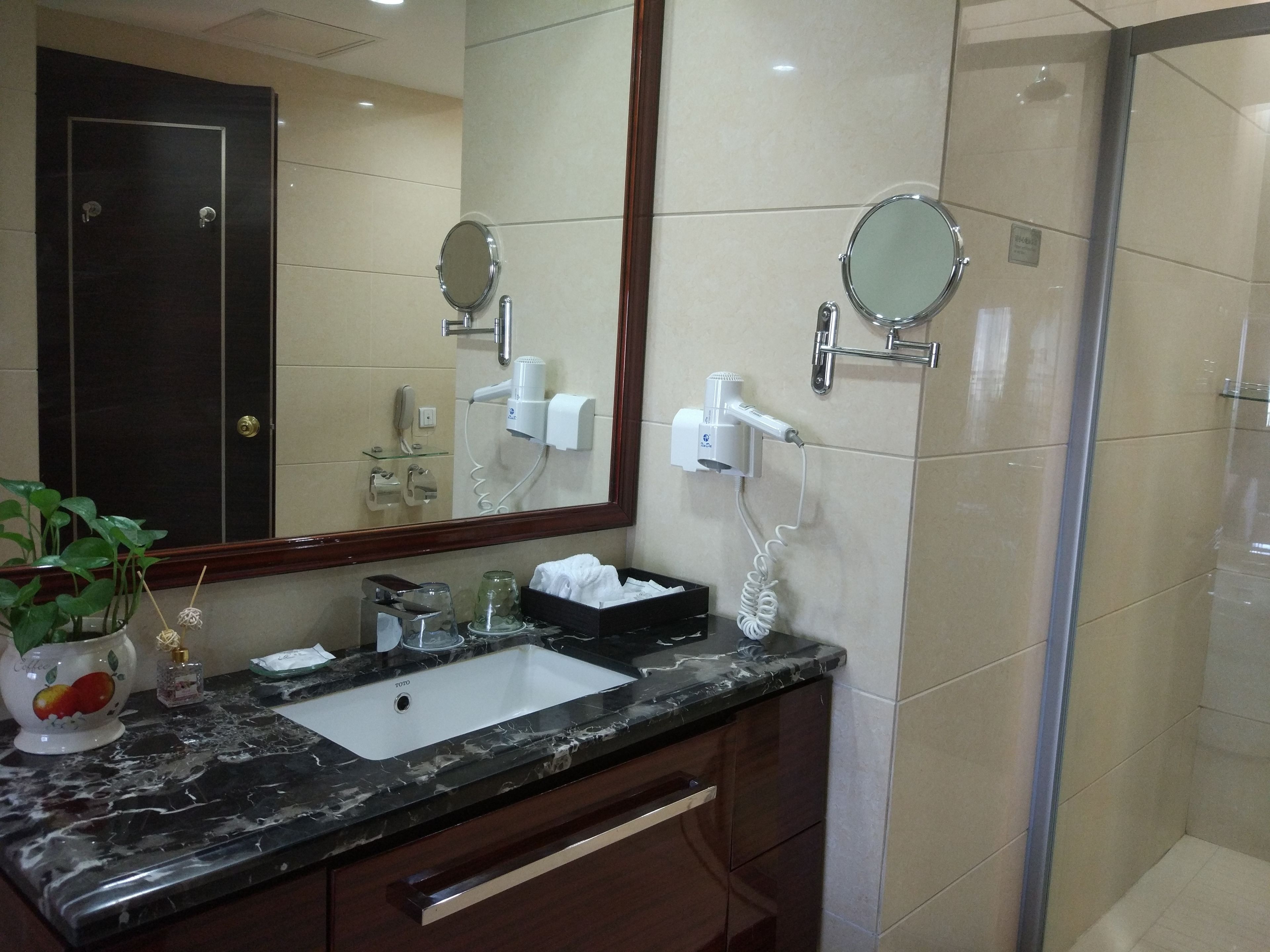 A bathroom with a marble sink, a large mirror, a hairdryer, and a glass shower enclosure.