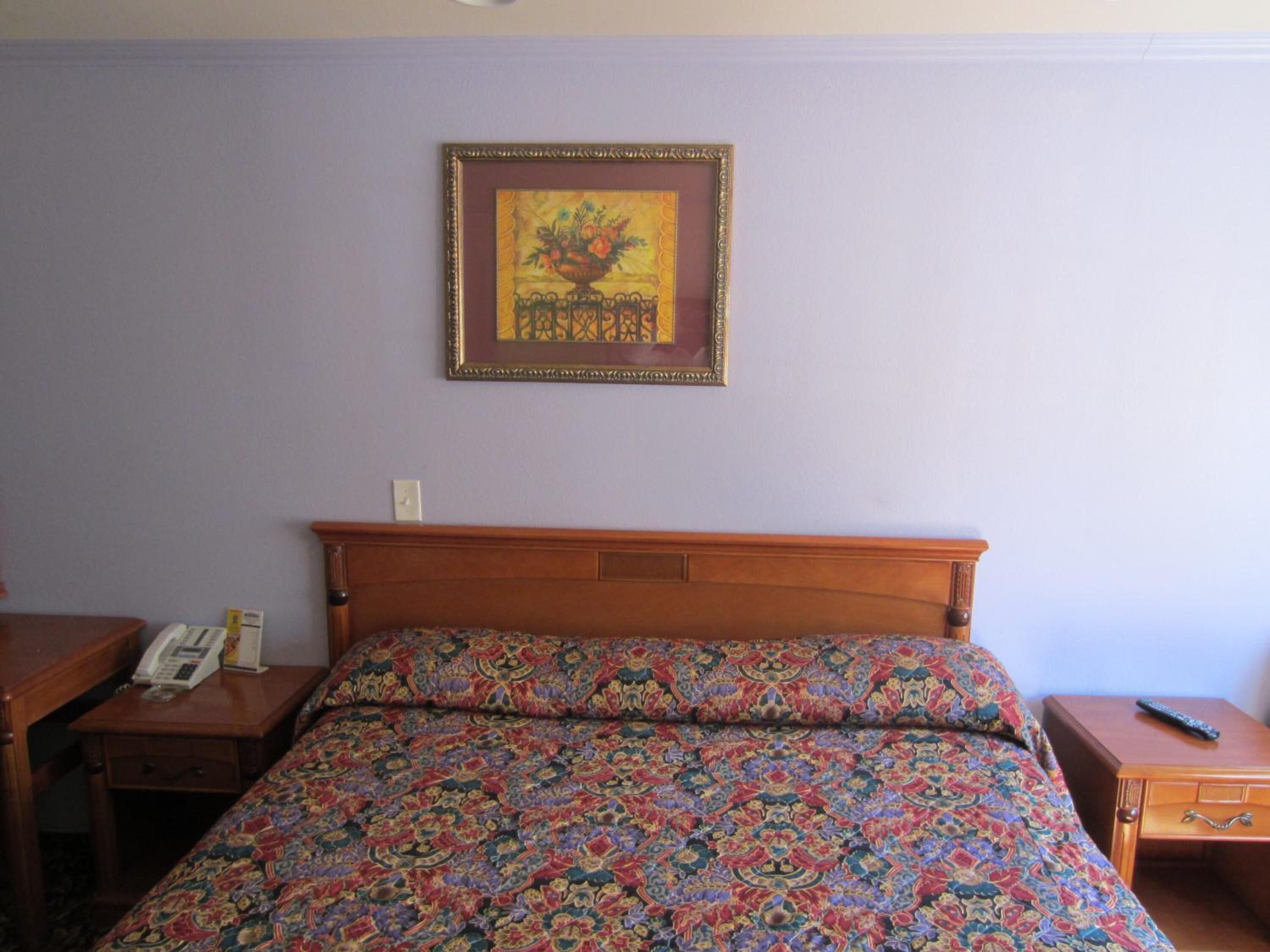 A hotel room with a wooden bed, a bedside table with a telephone, and a nightstand with a remote control.