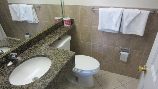 A bathroom with a granite countertop sink, a toilet, and a mirror. There are two white towels hanging on a towel rack. - Starlight Inn Canoga Park (Winnetka)