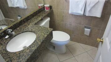 A bathroom with a granite countertop sink, a toilet, and a mirror. There are two white towels hanging on a towel rack.