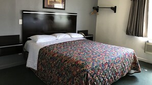 A hotel room with a large bed, a headboard, a bedside table with a lamp, a framed picture on the wall, and a window with curtains. - Starlight Inn Canoga Park (Winnetka)