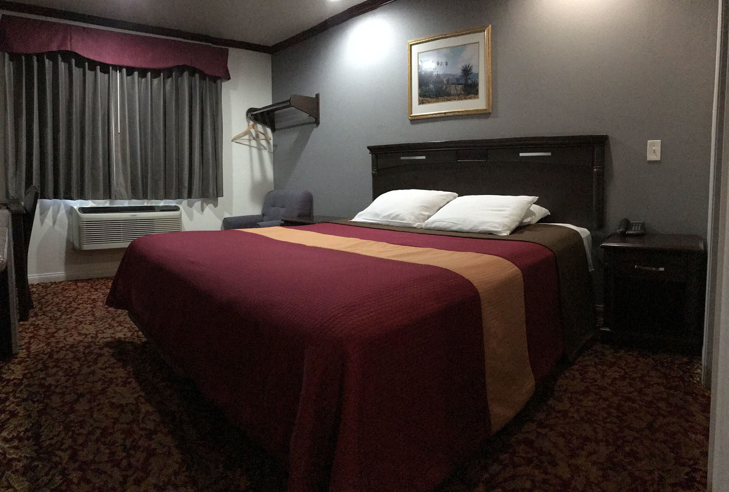 A hotel room with a large bed, a desk, a chair, a bedside table, a lamp, and a painting on the wall.