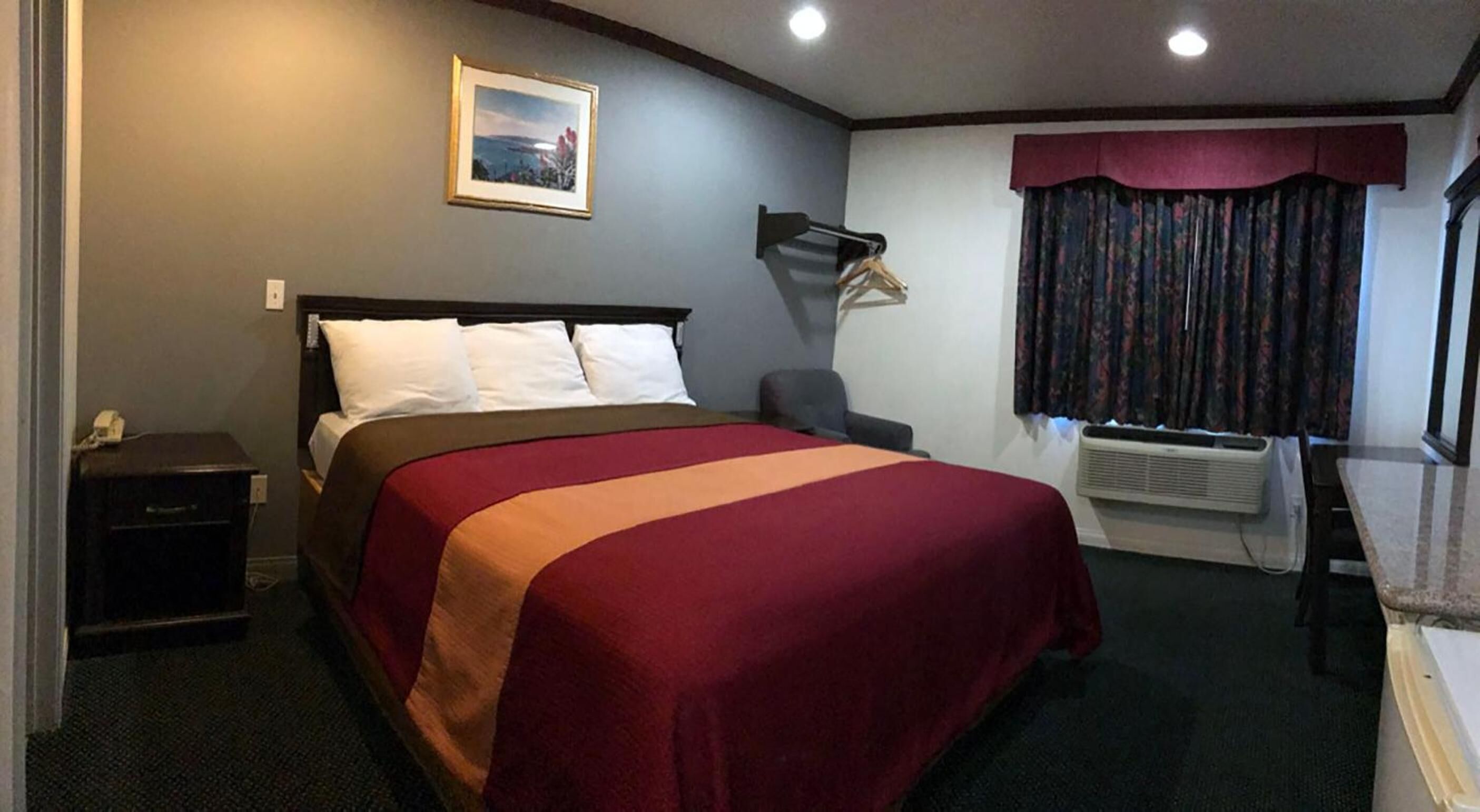 Ett hotellrum med en säng, ett skrivbord, en stol, en tavla på väggen och ett fönster med gardiner.