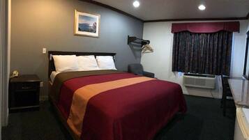 Ett hotellrum med en säng, ett skrivbord, en stol, en tavla på väggen och ett fönster med gardiner.