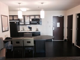 Cocina moderna con una isla central, muebles negros, microondas y refrigerador. Hay dos lámparas colgantes sobre la isla.