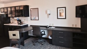 Une chambre d’hôtel équipée d’une kitchenette, d’un bureau, d’une chaise, d’un lit et d’un téléviseur.