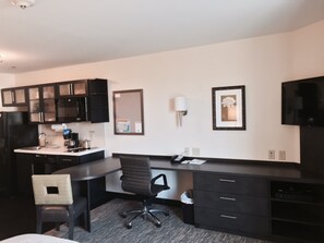 Une chambre d’hôtel équipée d’une kitchenette, d’un bureau, d’une chaise, d’un lit et d’un téléviseur.