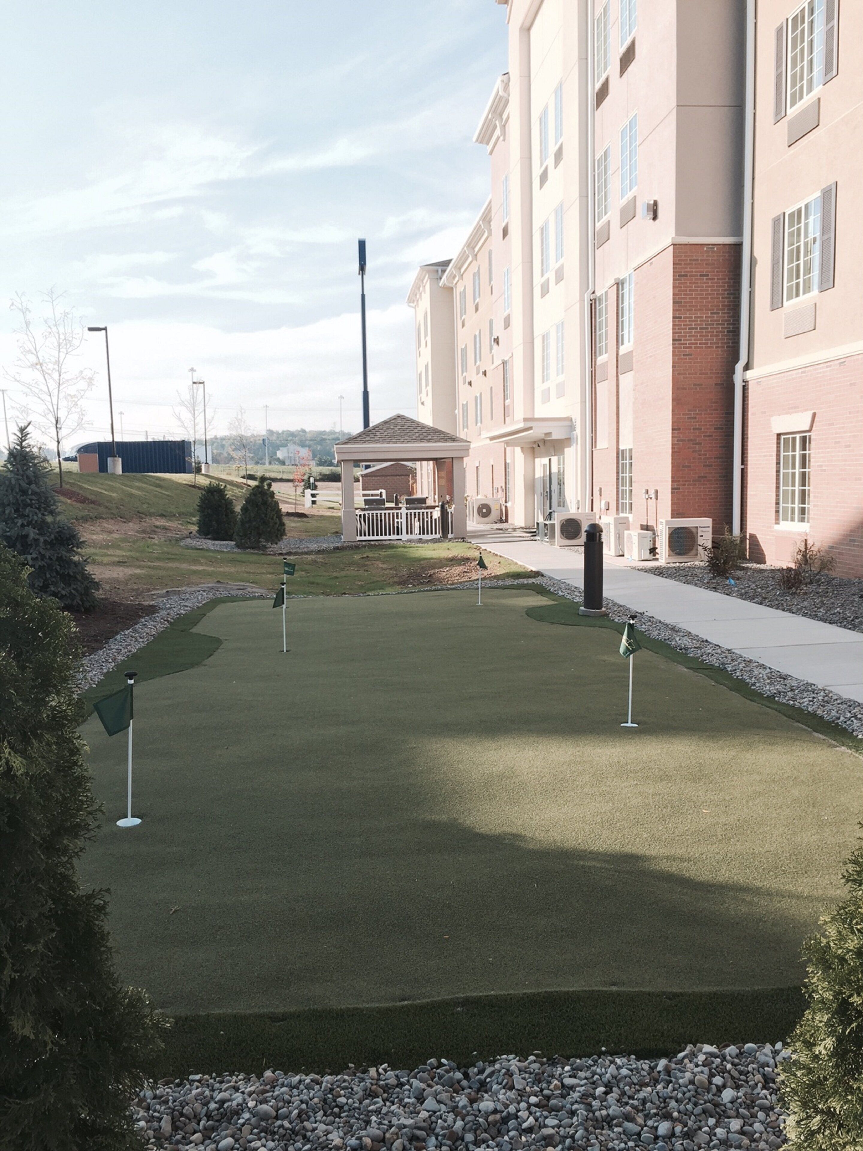Un campo de golf con un pabellón, un edificio con amplias ventanas y un cielo despejado.