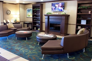 A hotel lobby with leather sofas, a fireplace, a television, and a bookshelf.