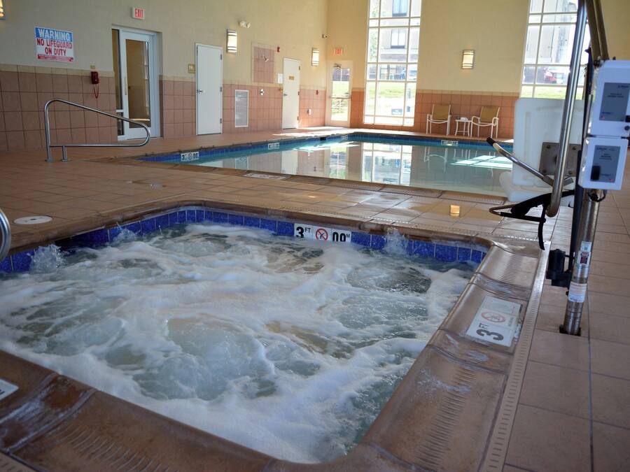 Jacuzzi con borde de azulejos, piscina al fondo y cartel que indica que no hay socorrista de servicio.