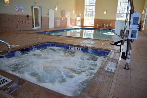 Jacuzzi con borde de azulejos, piscina al fondo y cartel que indica que no hay socorrista de servicio.