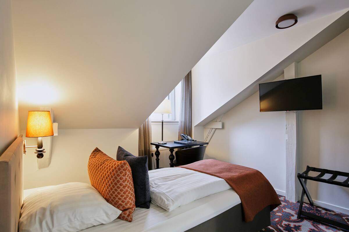 A hotel room with a bed, a desk, a chair, a TV, and a lamp.